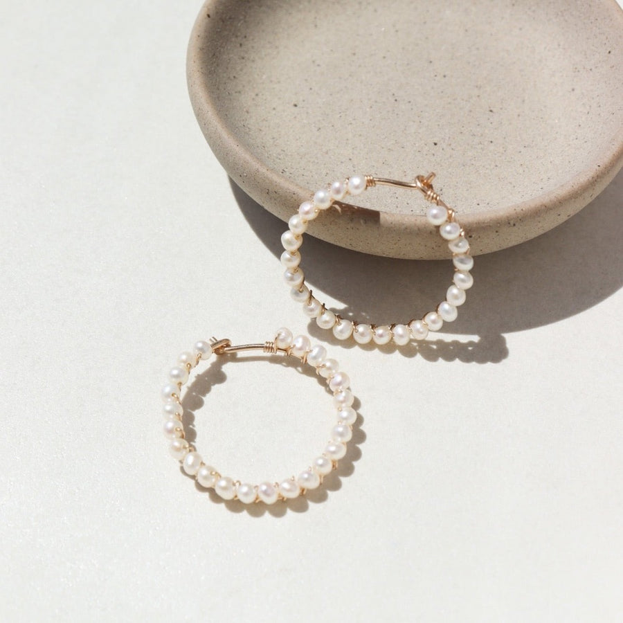 14k gold fill Pearl halo hoops laid against a tan plate in the sunlight.