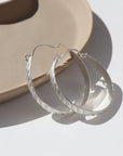 Sterling silver ripple hoops resting on a brown ceramic dish