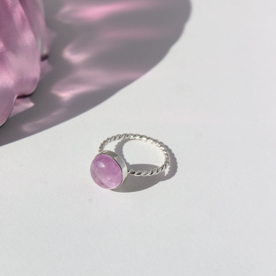 925 Sterling Silver Pippa Ring laid on a white paper in the sunlight. This ring features a sprial band with a pink kunzite gemstone.  