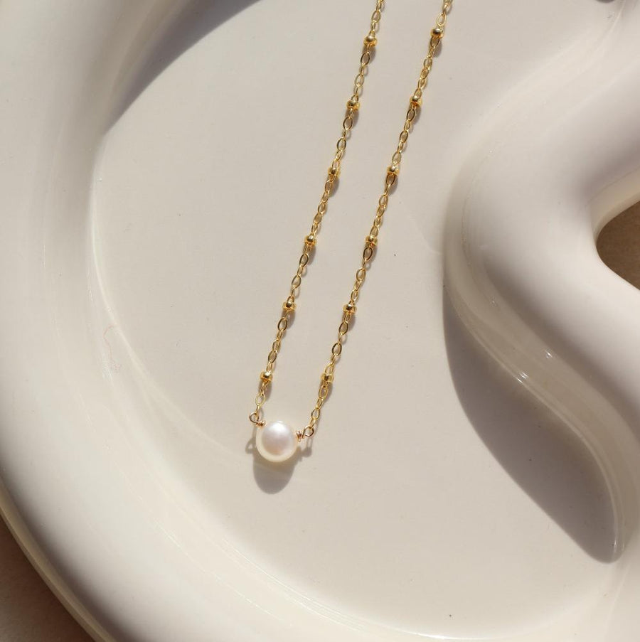 14k gold fill Beaded pearl necklace laid on a white plate in the sunlight. 