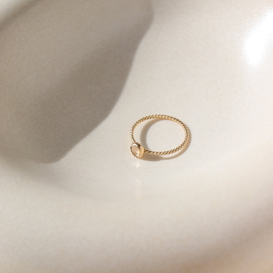 14k gold fill Gaia Ring laid on a white plate in the sunlight. This ring features a Spiral band with a zircon gemstone.
