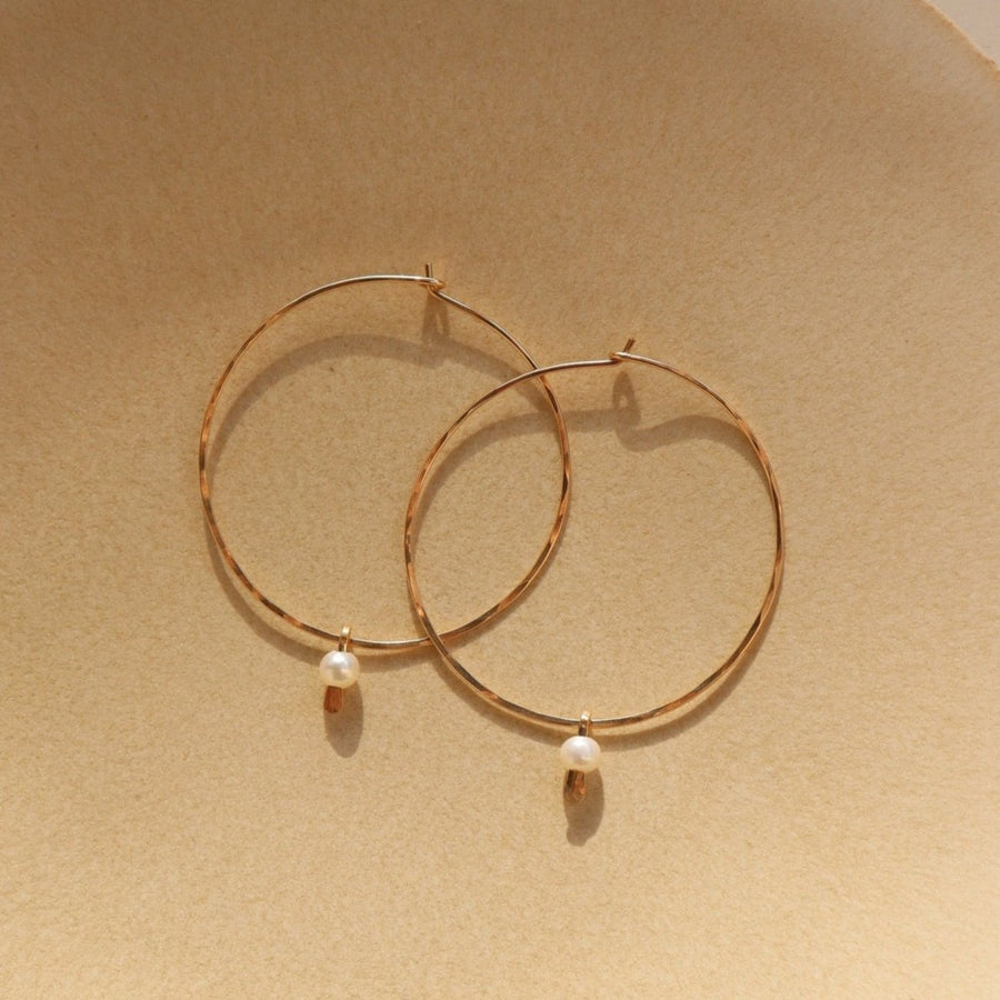 14k gold fill Emma pearl hoops laid on a tan plate in the sunlight