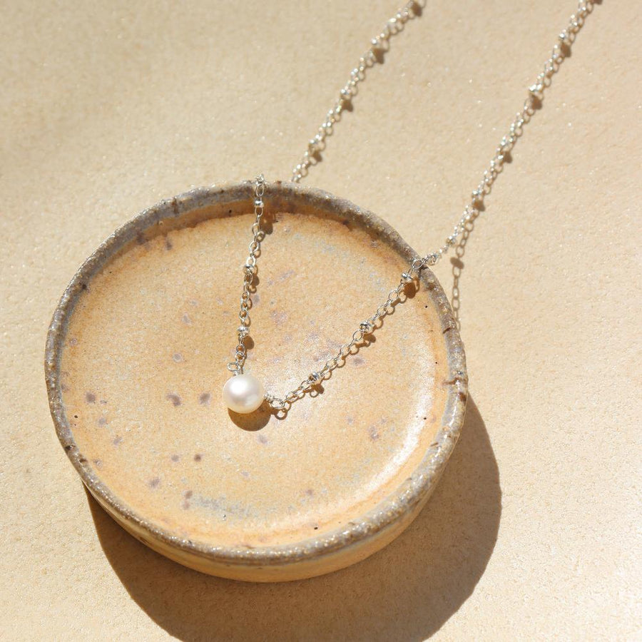 925 sterling silver beaded chain with a pretty single pearl necklace laid on a white plate in the sunlight. 