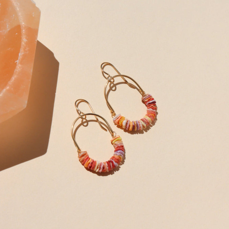 Gold hoop earrings with colorful beads on a beige background