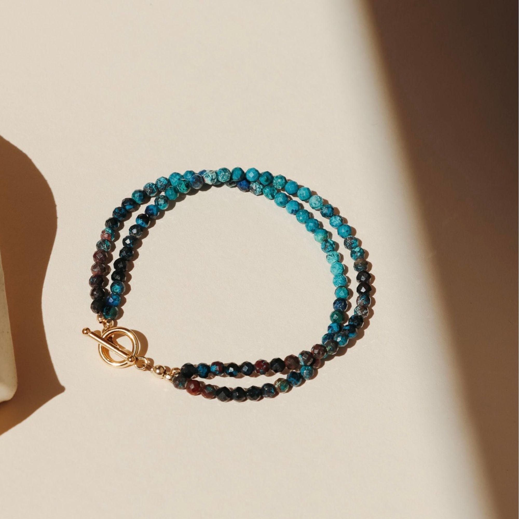 chrysocolla beaded gemstone bracelet with a toggle closure on a beige background in the sunlight