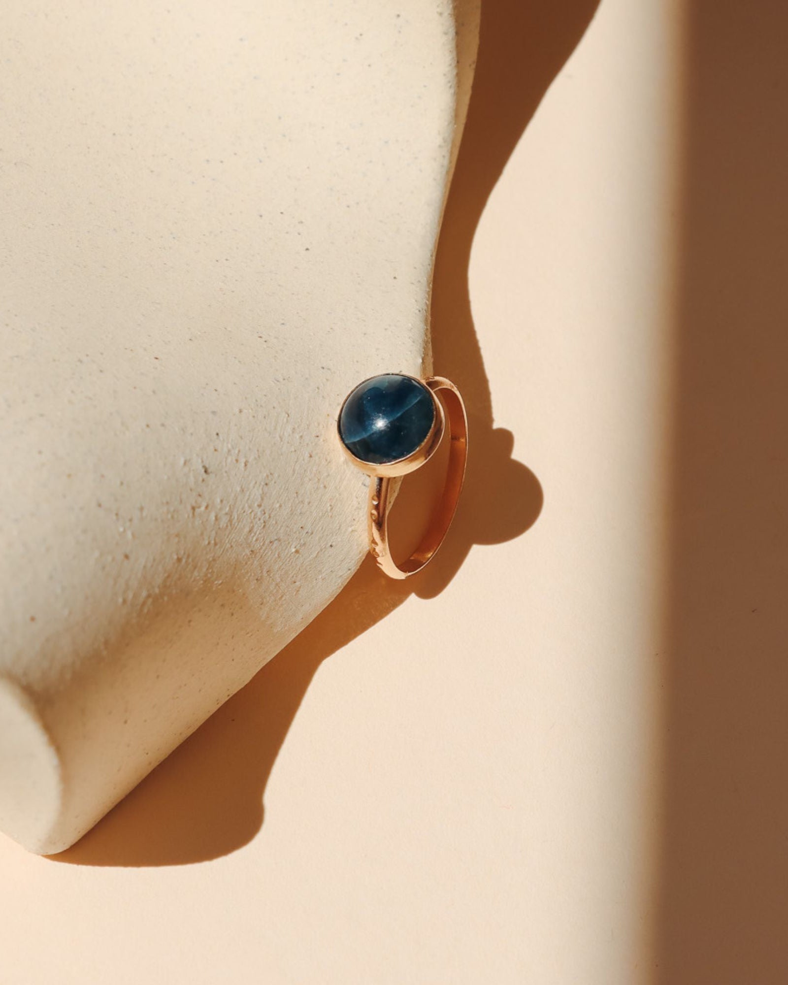 14k gold fill ring with round blue stone on a light dish