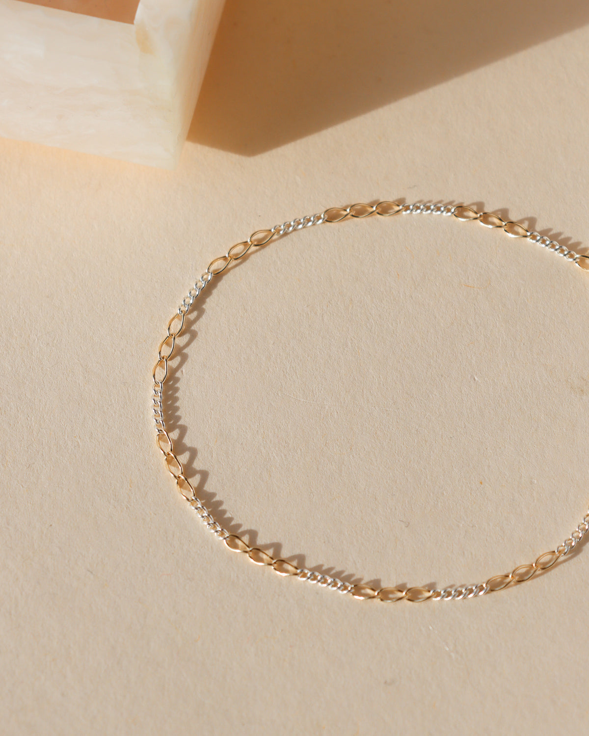 Interlude Bracelet featuring alternating 14k gold fill elongated links and sterling silver chain links, photographed in warm sunlight on a neutral background.