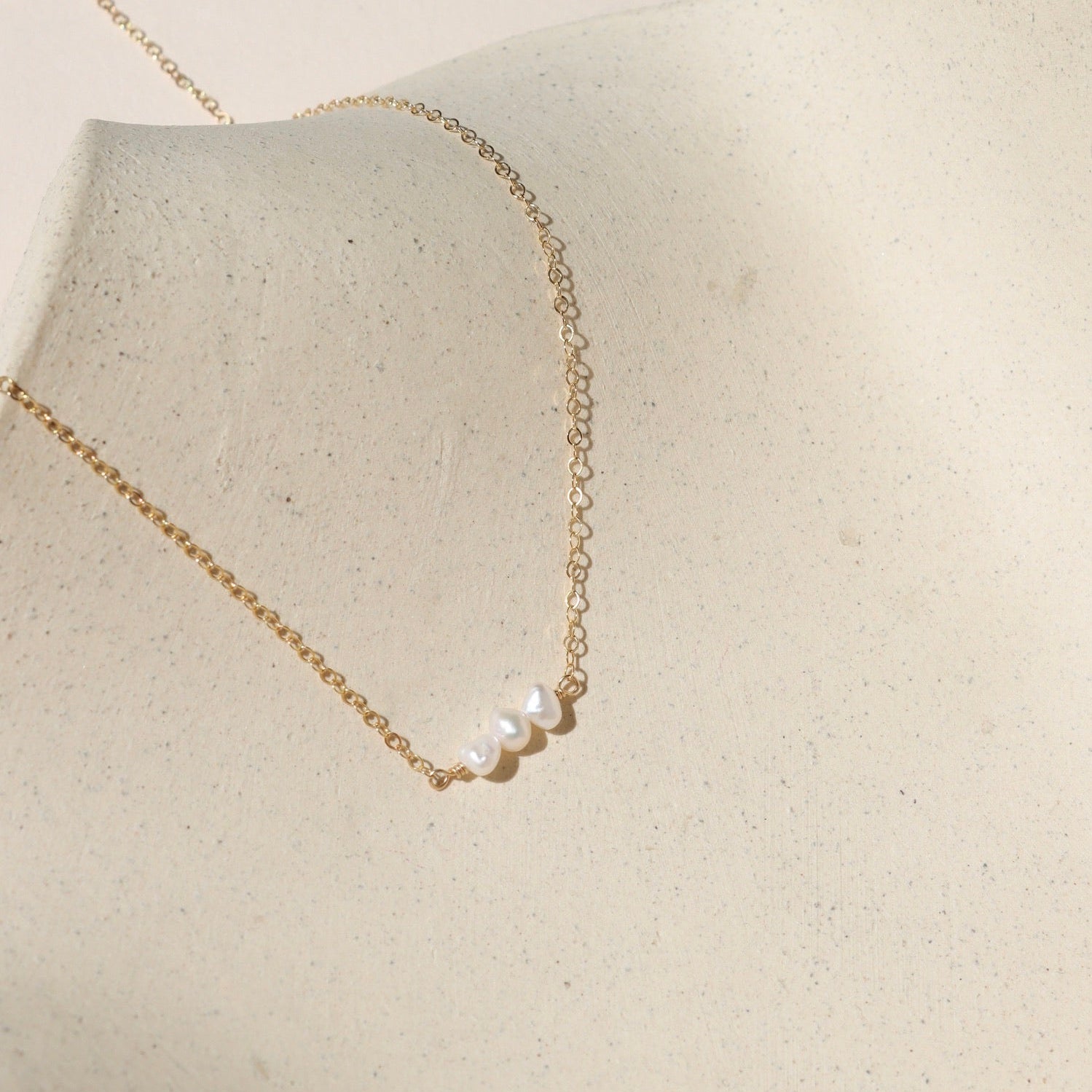 14k gold fill delicate chain necklace with 3 fresh water pearls on a light dish