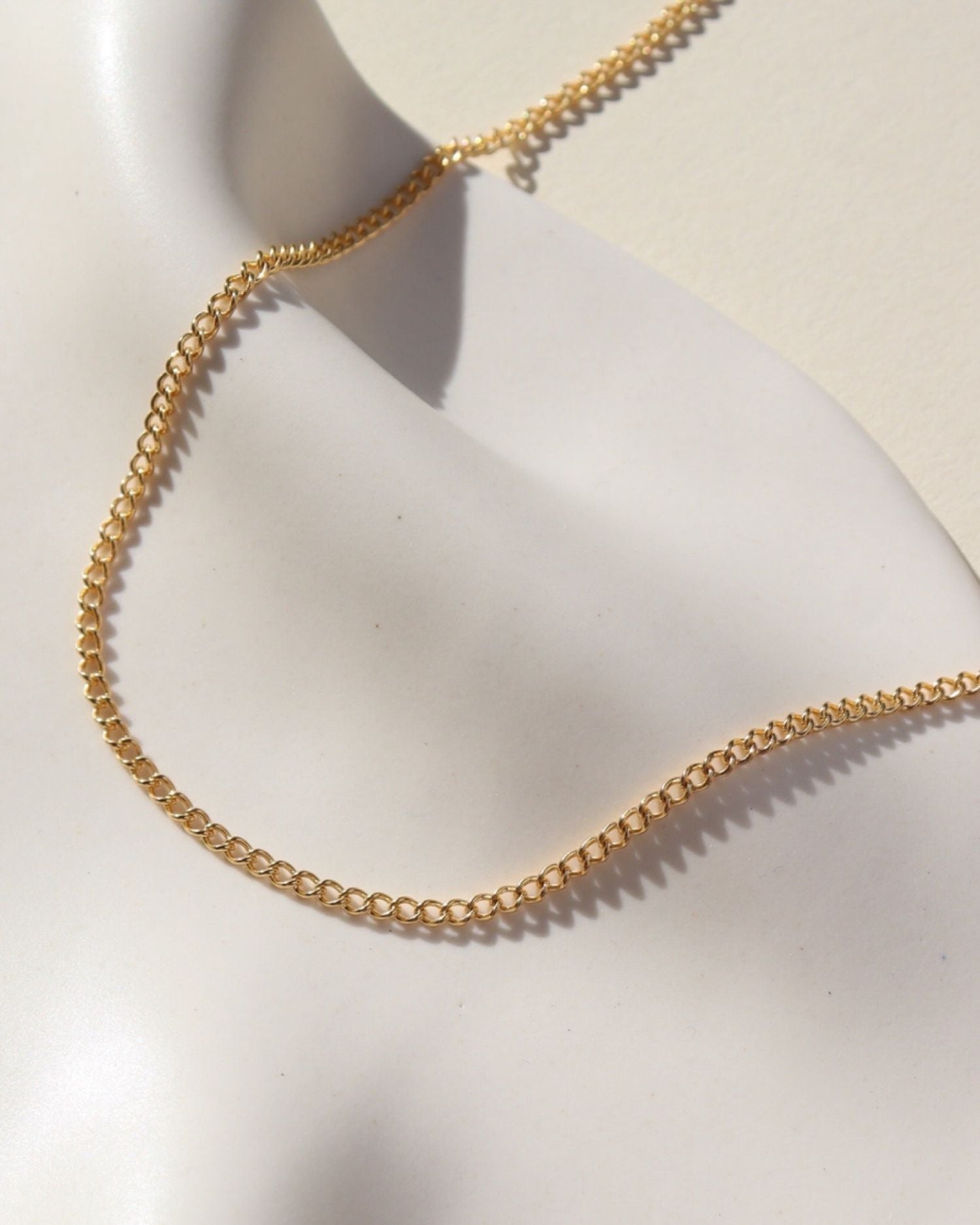 La Mer Necklace in 14k gold fill on a white plate in the sunlight.