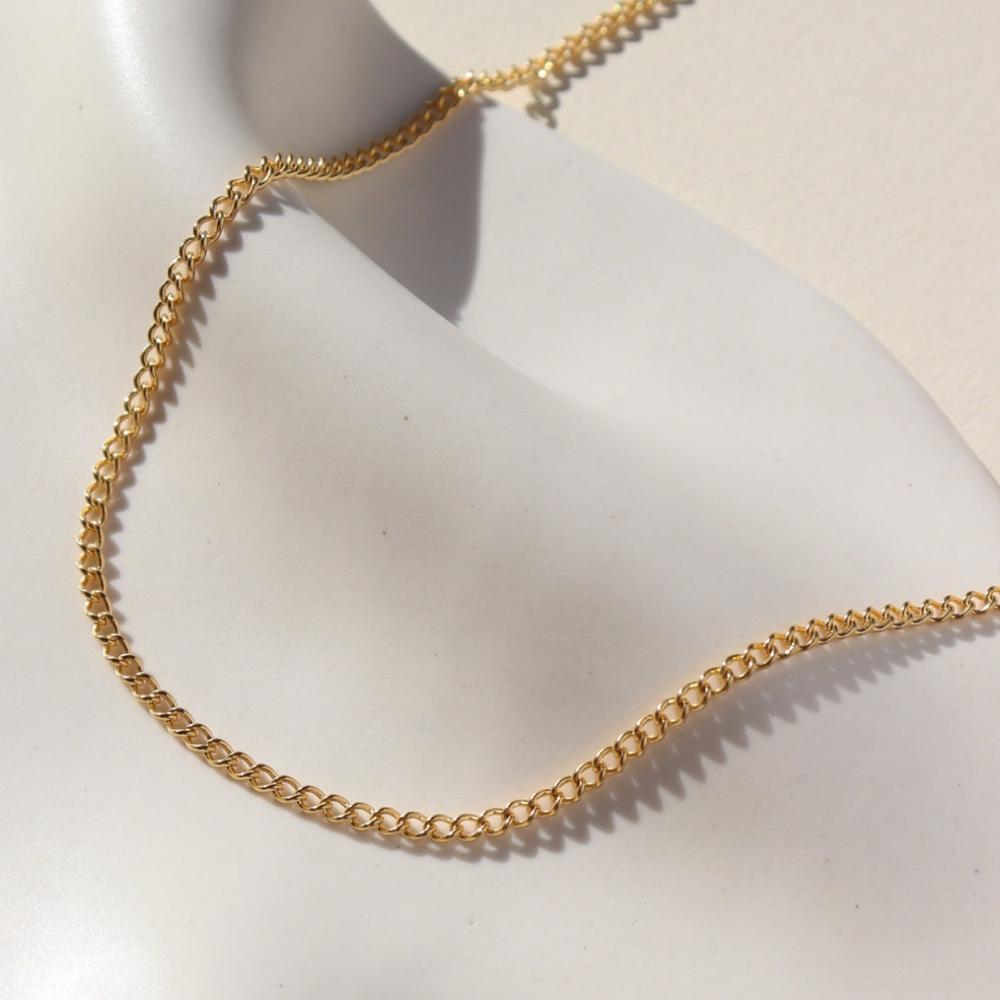 La Mer Necklace in 14k gold fill on a white plate in the sunlight.