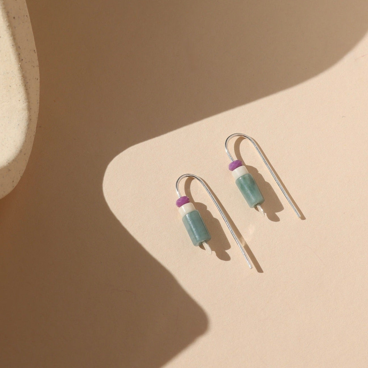 sterling silver threader earrings with faceted phosphosiderite, fossil jasper, and guatamalan jade on a light dish