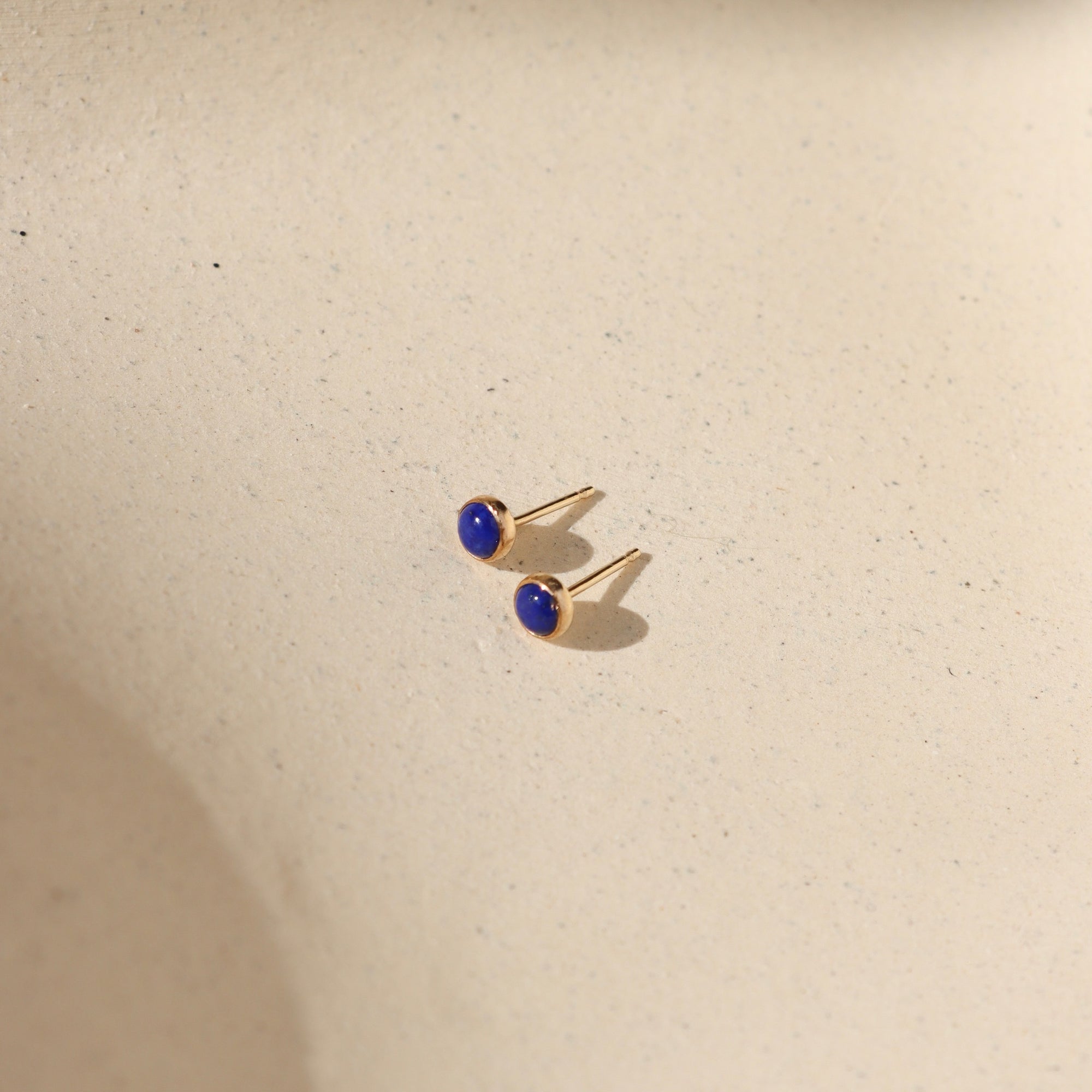 14k gold fill bezel ear posts with 4mm lapis lazuli stones on a light background