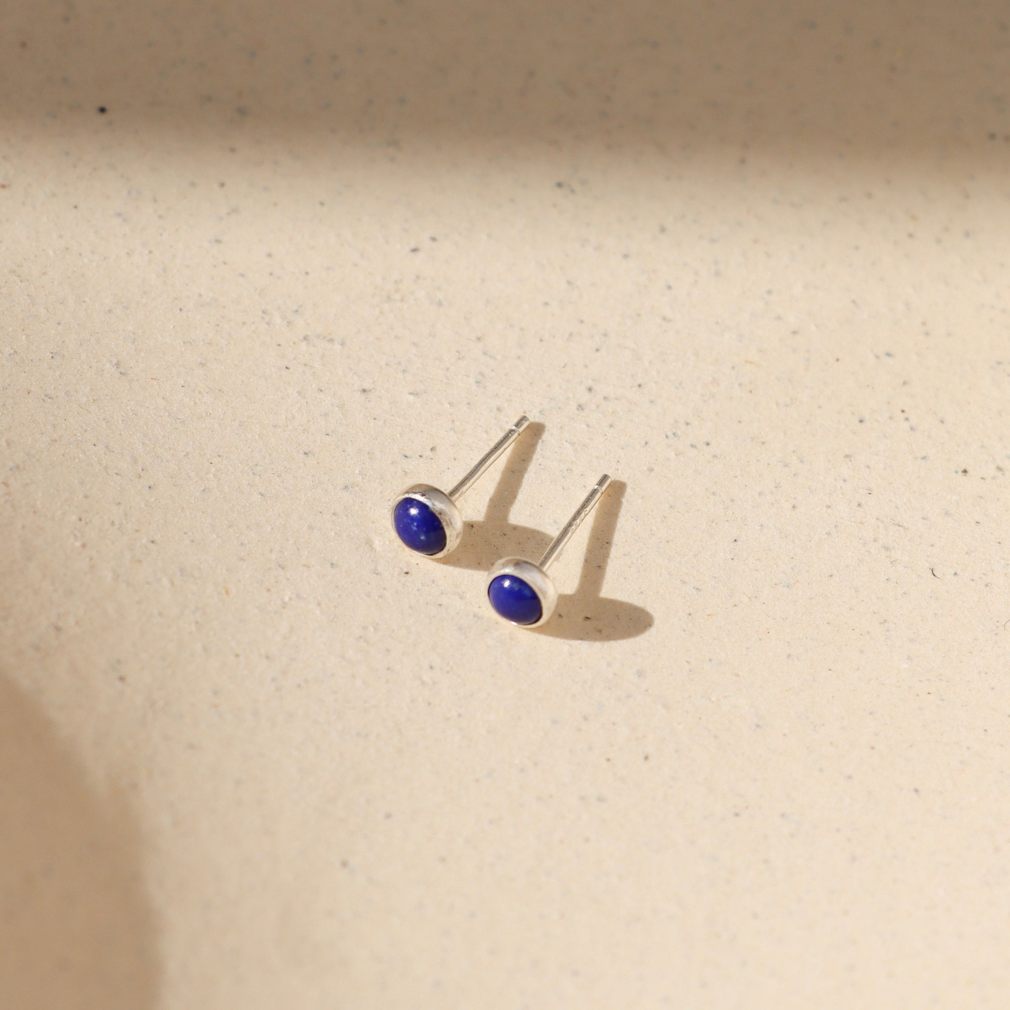 sterling silver ear posts with 4mm lapis lazuli stones on a light background