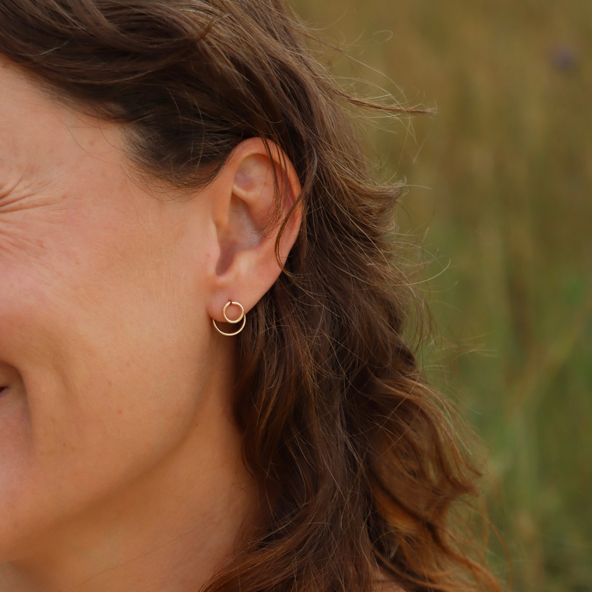 Close-up of a gold double hoop earring worn on the ear, styled outdoors.
