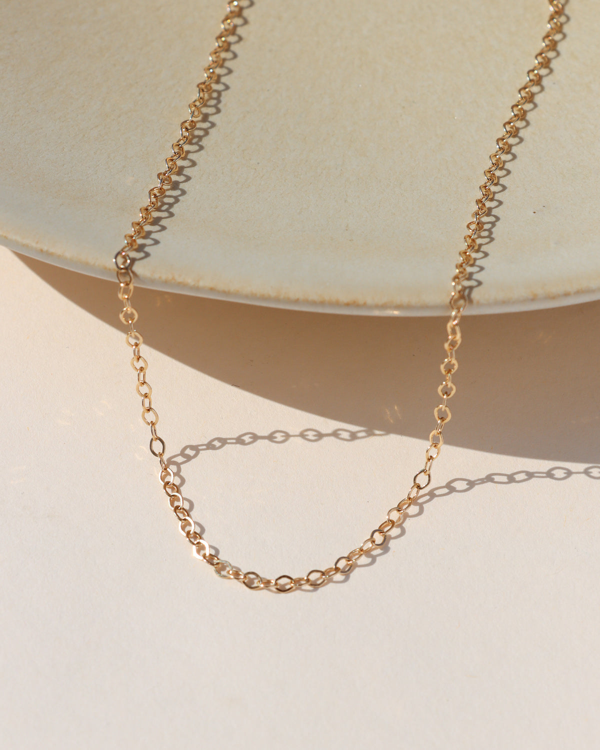 Delicate gold-filled oval-link chain necklace displayed on a neutral surface in warm sunlight.