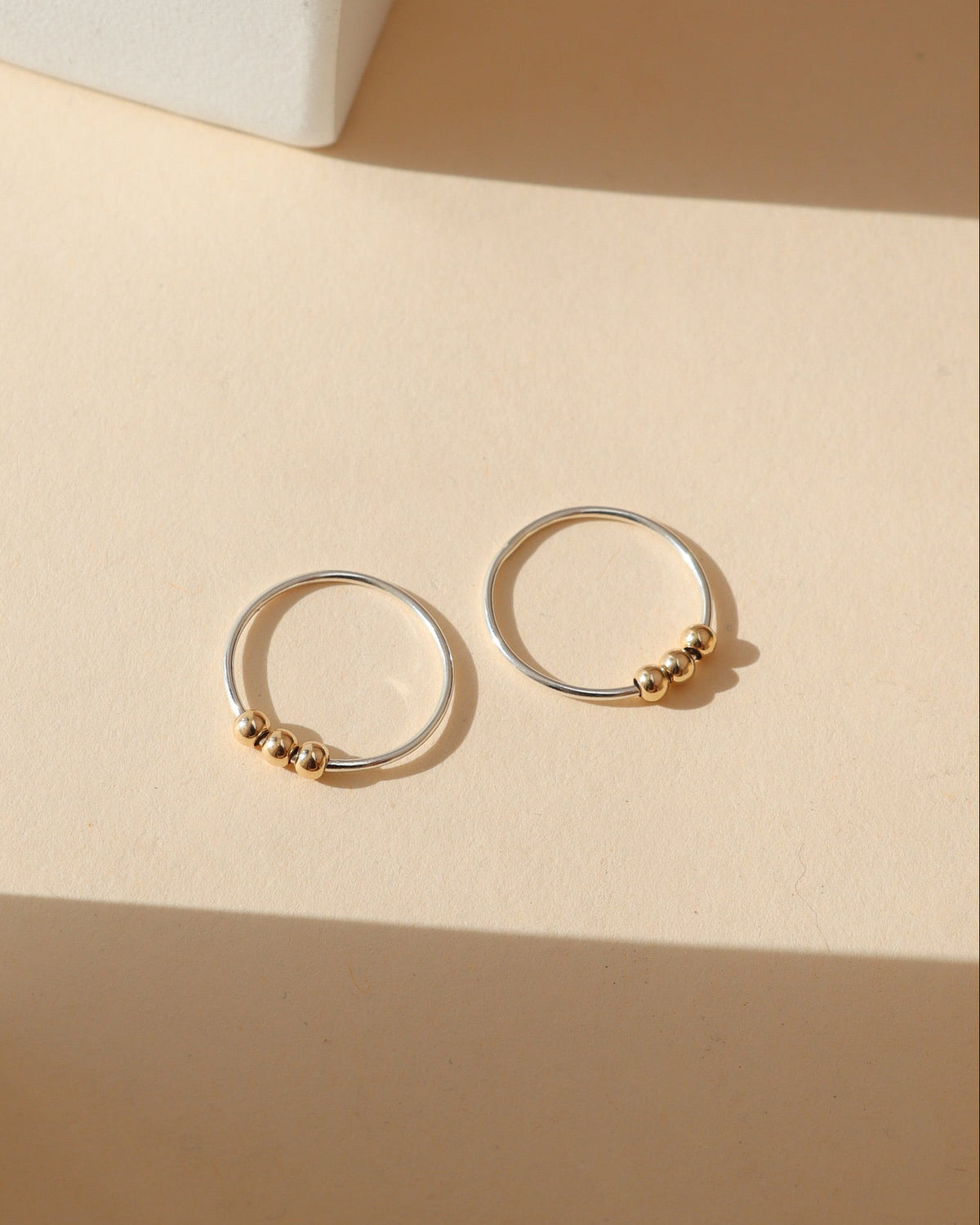 Pair of Token Jewelry mixed metal hoop earrings featuring thin sterling silver circular hoops accented with three polished gold beads, displayed on a cream background in natural sunlight.