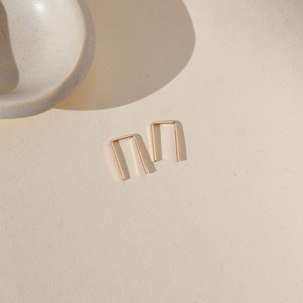 14k gold fill mini staple shaped earrings laid by small dish in the sunlight
