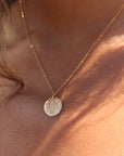 Model wearing 14k gold fill sun drop necklace in the sunlight. This necklace features our simple chain met by a hammered coin, making it look like the moon.