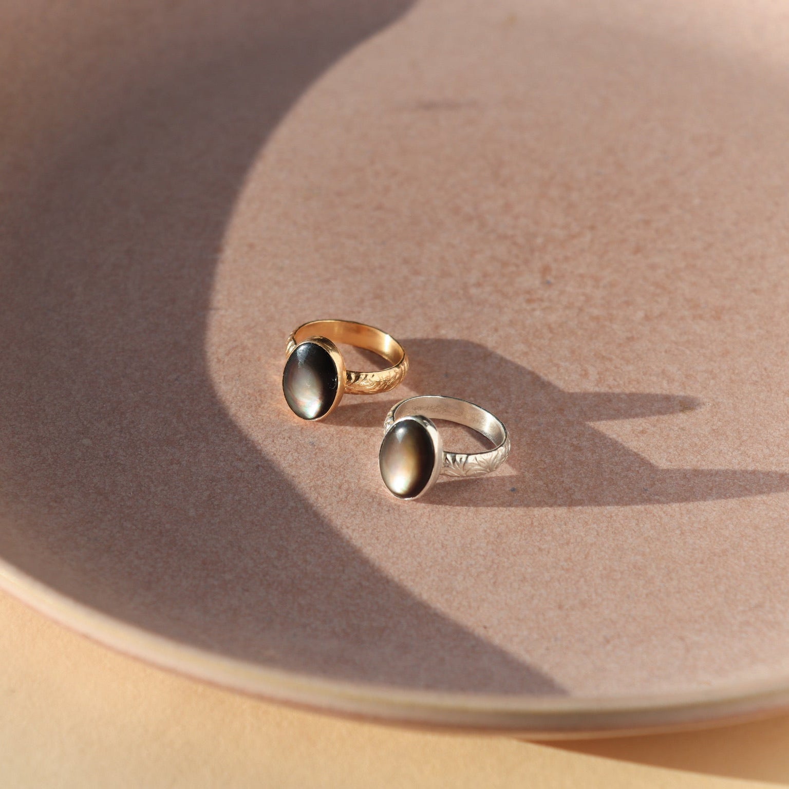 Moonflower rings in gold and silver with oval luminous stones, styled on a neutral surface in soft natural light.