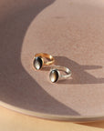 Moonflower rings in gold and silver with oval luminous stones, styled on a neutral surface in soft natural light.
