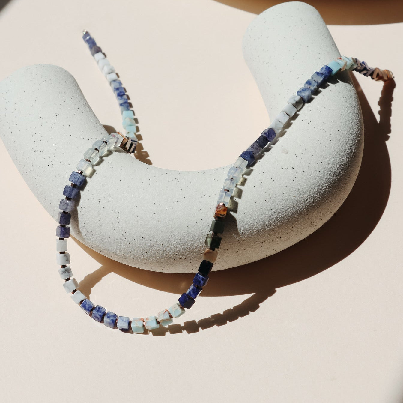 Beaded necklace draped on a beige arc dish in the sunlight.