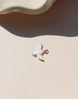 A small iridescent mother-of-pearl bird charm with a gold-toned loop, photographed on a cream-colored surface in sunlight.
