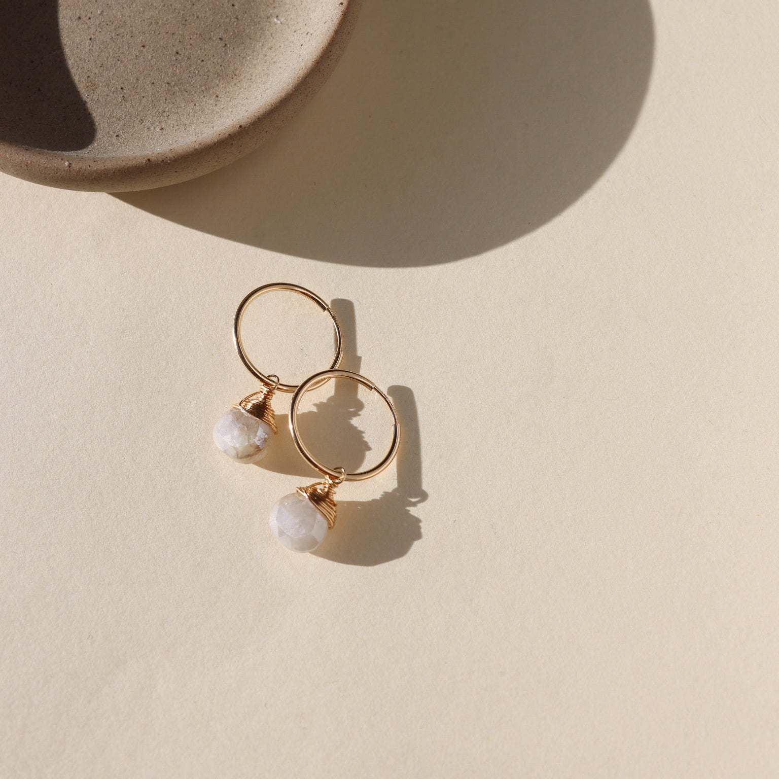 Gold hoop earrings featuring iridescent moonstone charms with soft, shimmering hues.