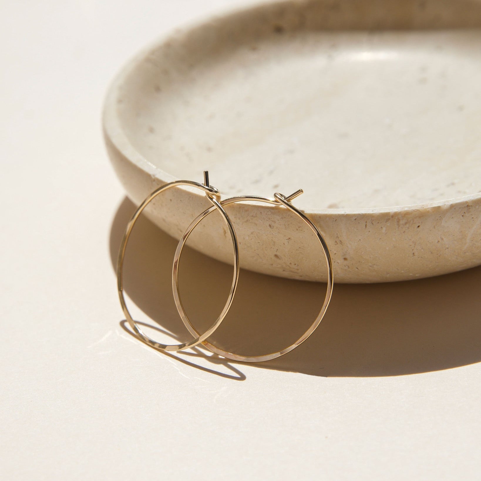 14k gold fill hammered hoop earrings on a light dish