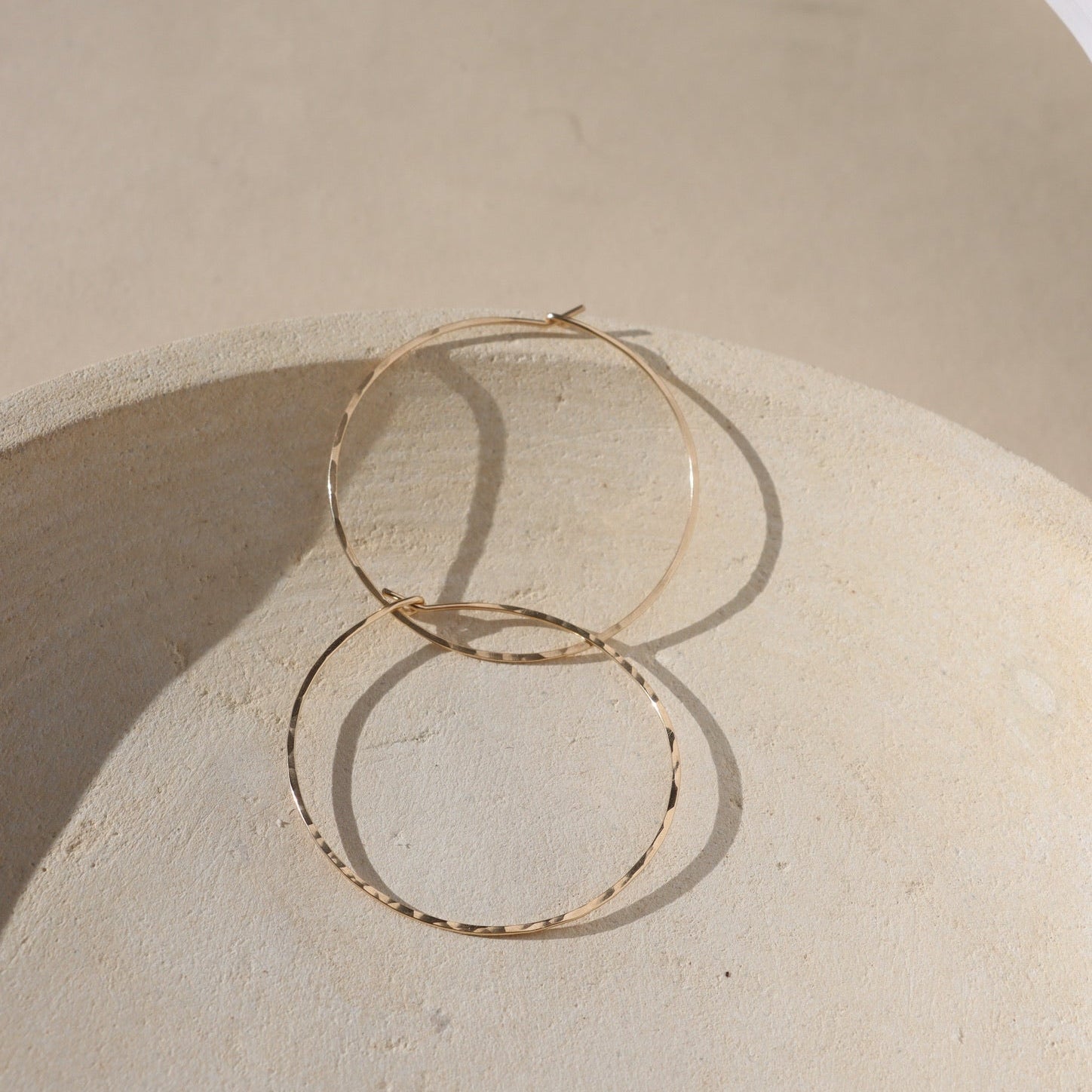 14k gold fill hammered hoop earrings on a light dish