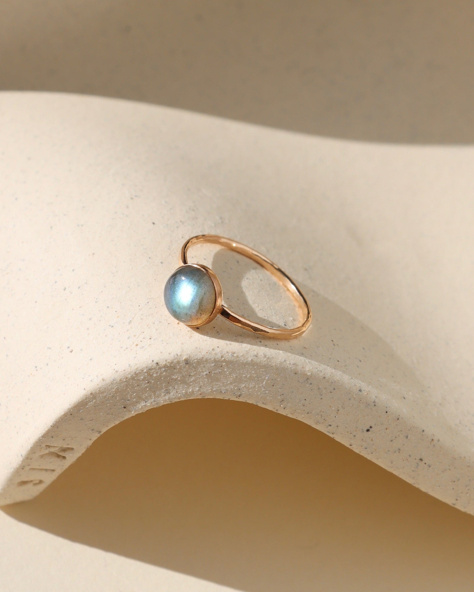 Gold ring with a blue gemstone on a beige stone surface