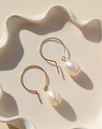 A pair of pearl earrings resting on a white, wavy ceramic dish in natural light.