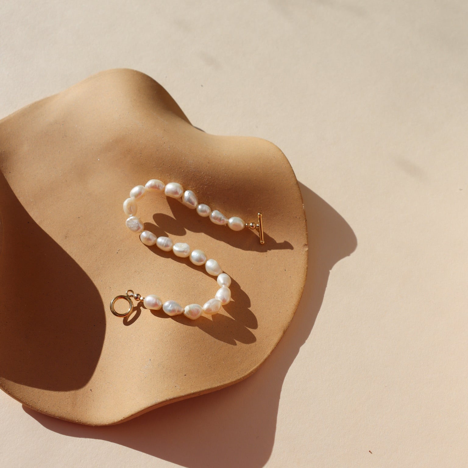 Gold toggle bracelet featuring a strand of lustrous freshwater pearls and a bold circular toggle clasp.