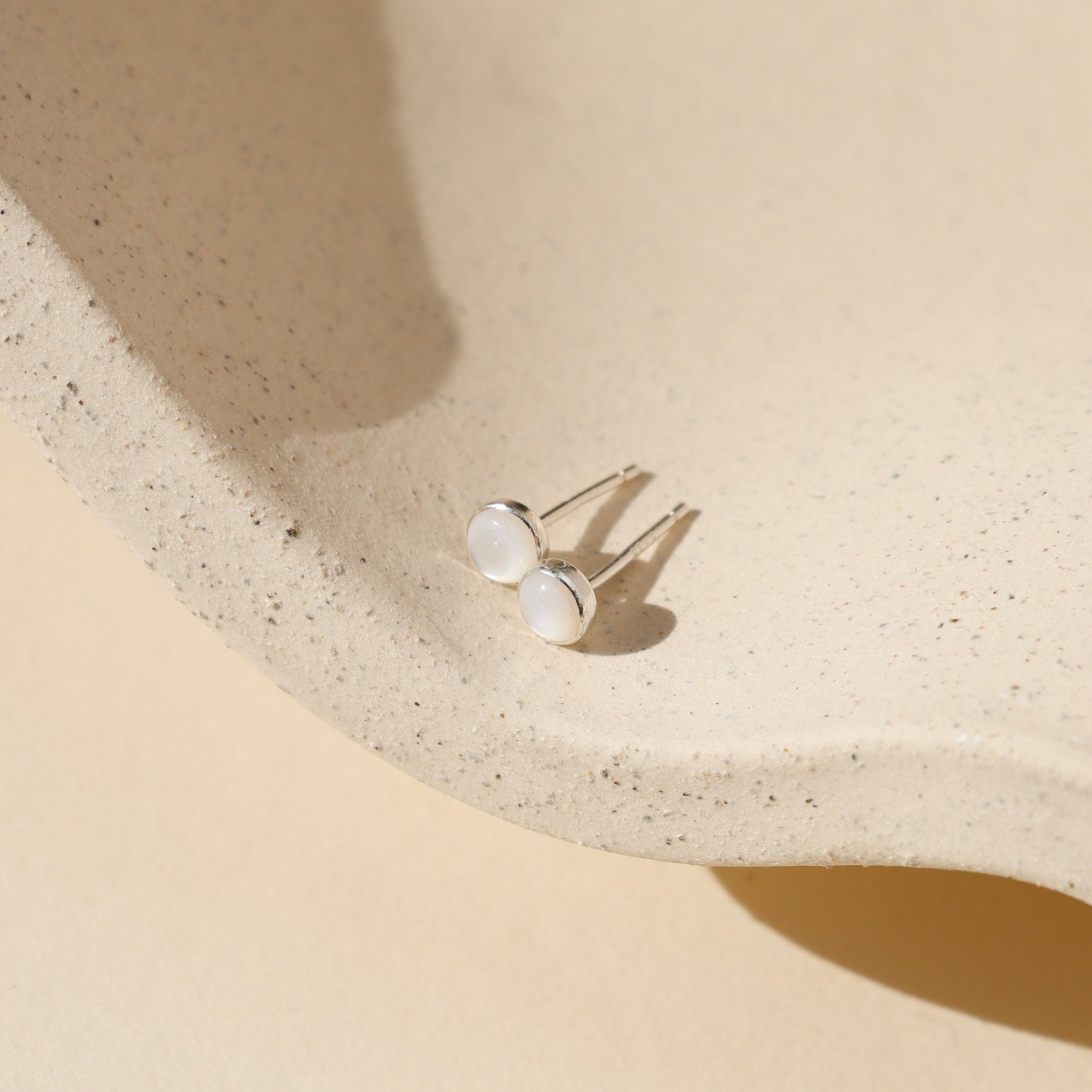 sterling silver bezel ear post with 4mm mother of pearl stone on a light dish