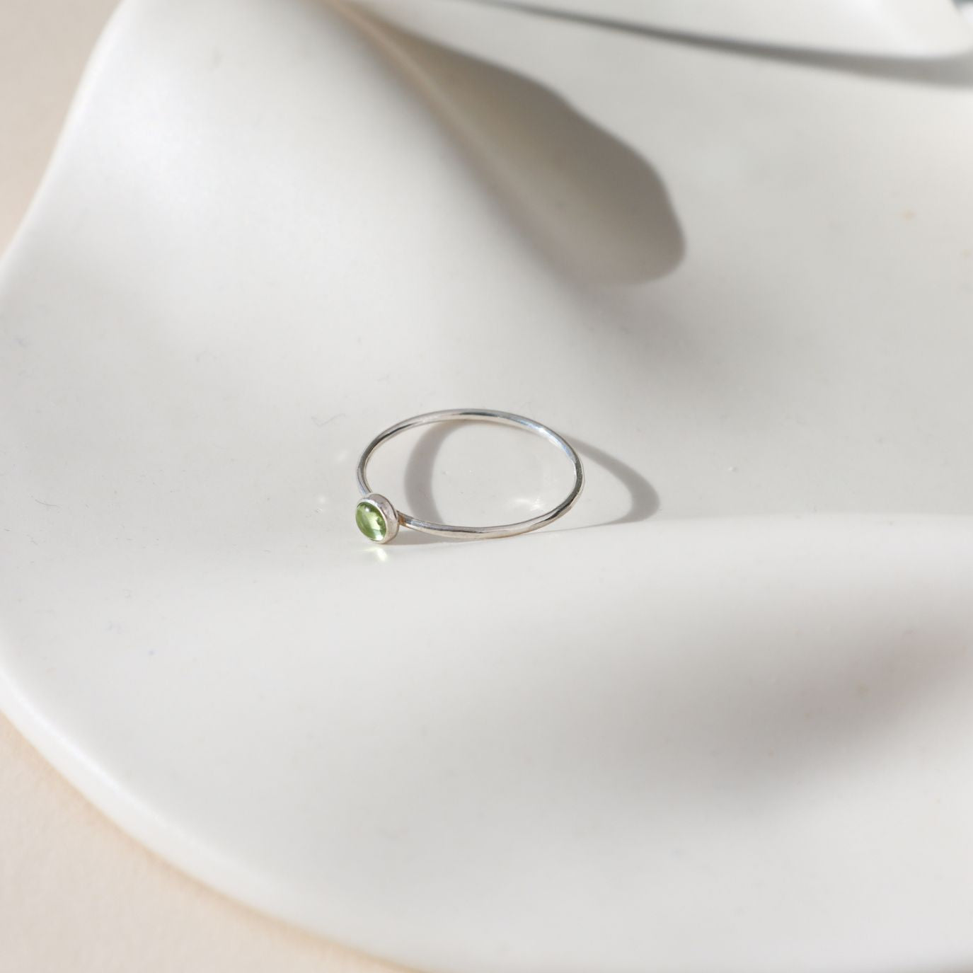 sterling silver bezel ring with 4mm peridot gemstone on a light dish