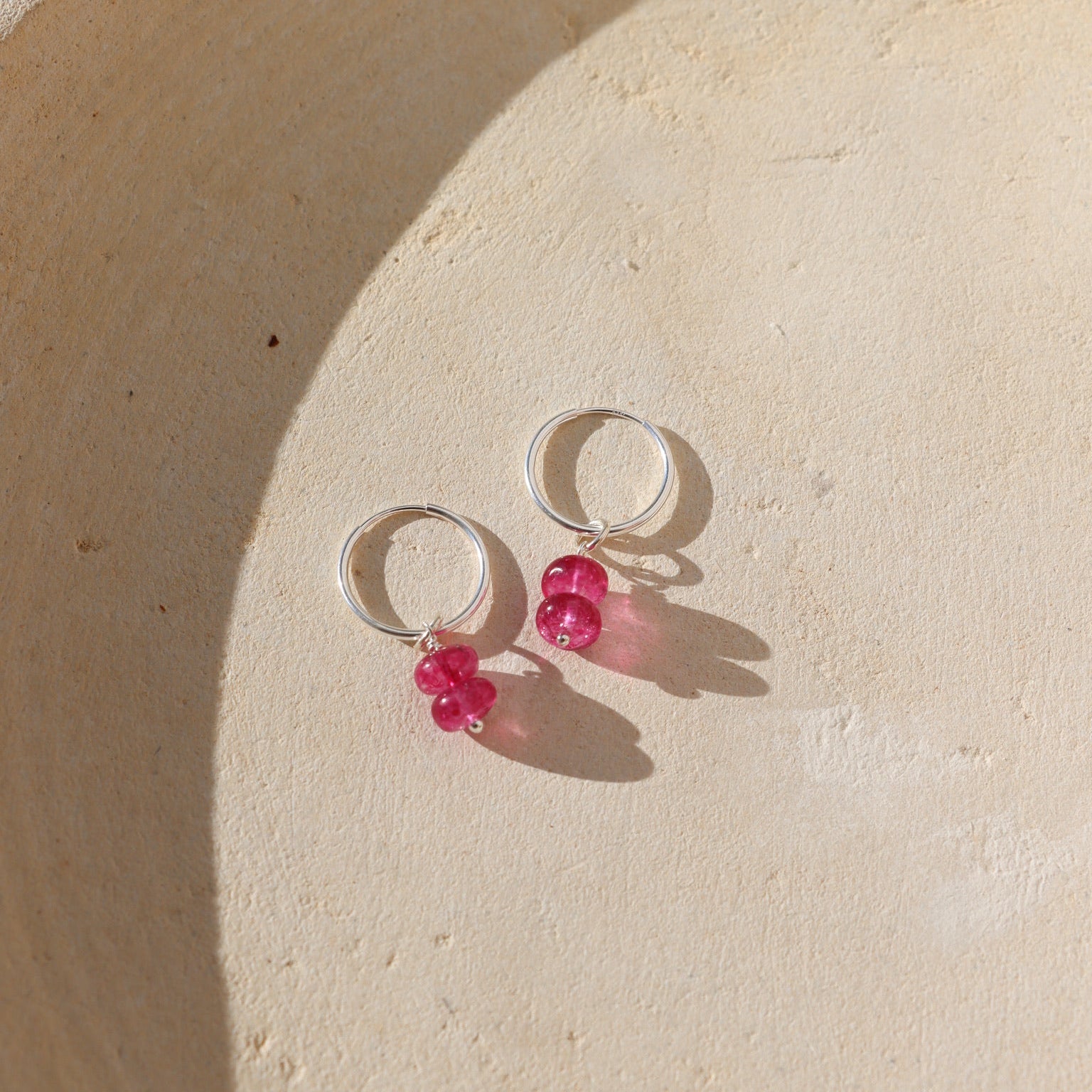 pink topaz charm in sterling silver shown on a simple sterling silver hoop earring in the sunlight
