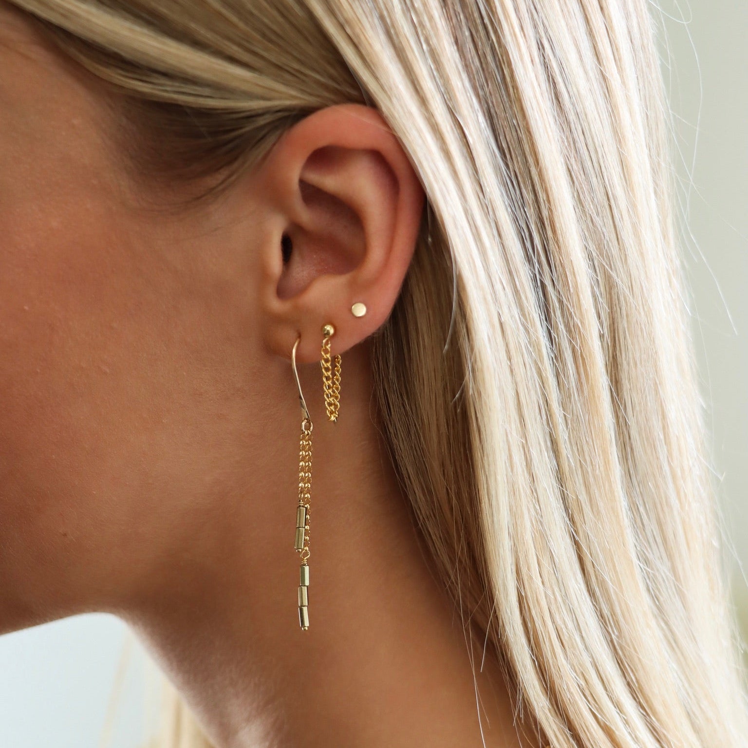Model wearing 14k gold fill threader earrings with delicate chain and bar drop details, styled with a 14k gold fill chain stud and classic gold dot stud in a minimal layered ear stack.