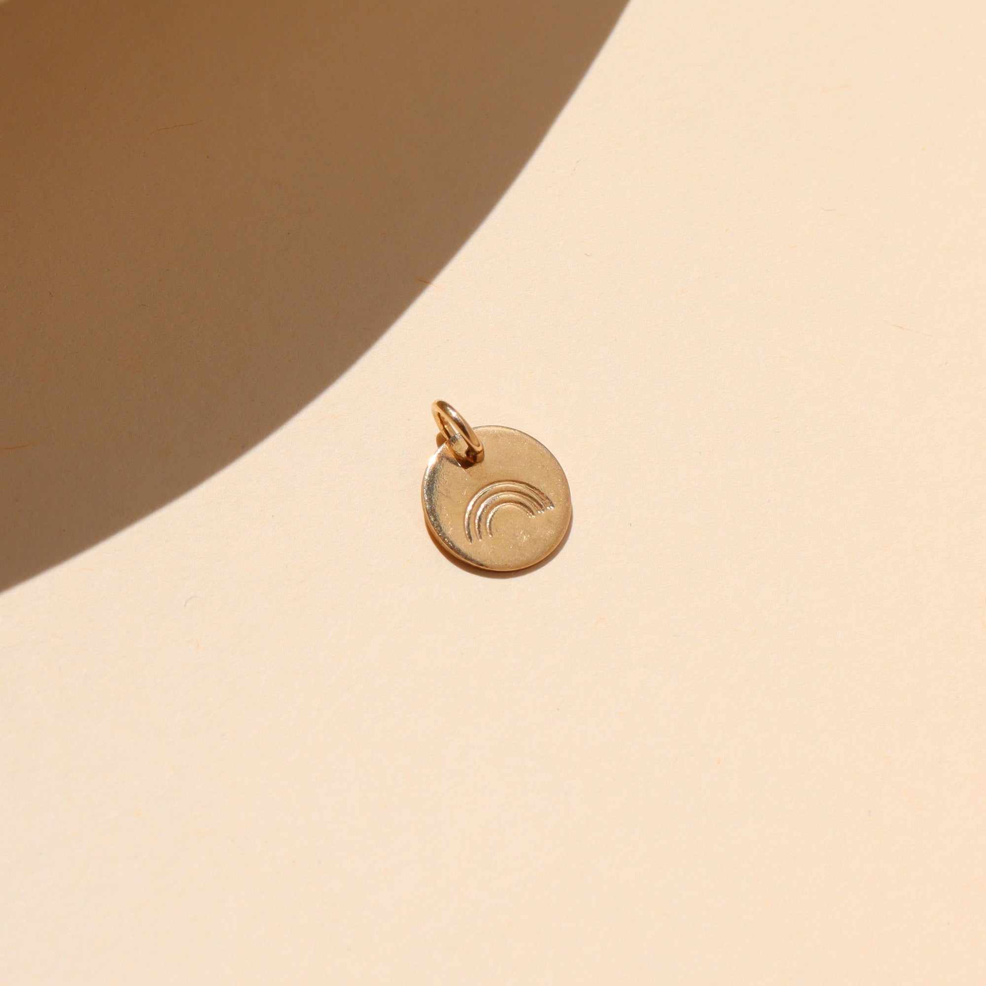 14k gold fill small disk with a rainbow stamp on a light dish

