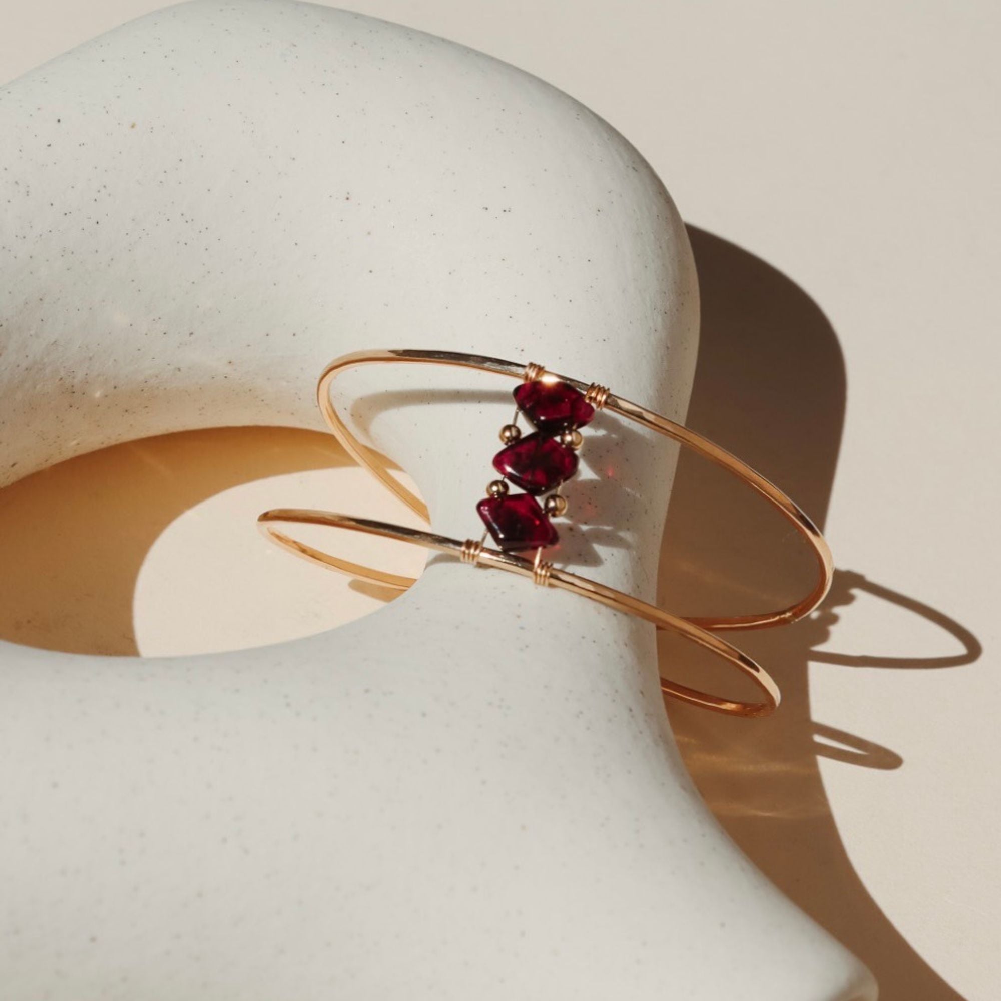 14k gold fill cuff bracelet with three ruby gemstones on a light dish