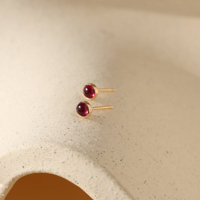 Gold filled bezel set earrings with July's birthstone, red Ruby gemstones on a ceramic dish