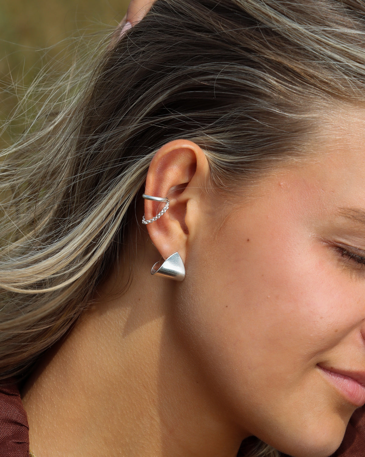 Sculptural sterling silver stud earrings with a dimensional folded silhouette, paired with a delicate chain ear cuff for an effortless layered look.