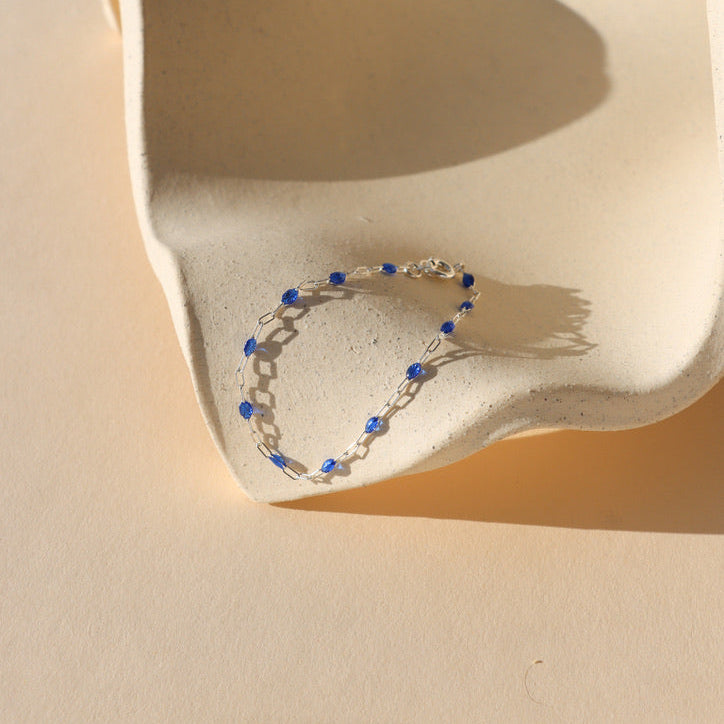 sterling silver chain alternating with transparent sapphire creating a dainty bracelet on a light dish