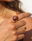 The Scarlett Ring, available in 14k gold fill or sterling silver, features a stunning Red Tiger Eye gemstone on a triple 14k gold fill band. It reflect light beautifully as the model wears it along with a hand chain.