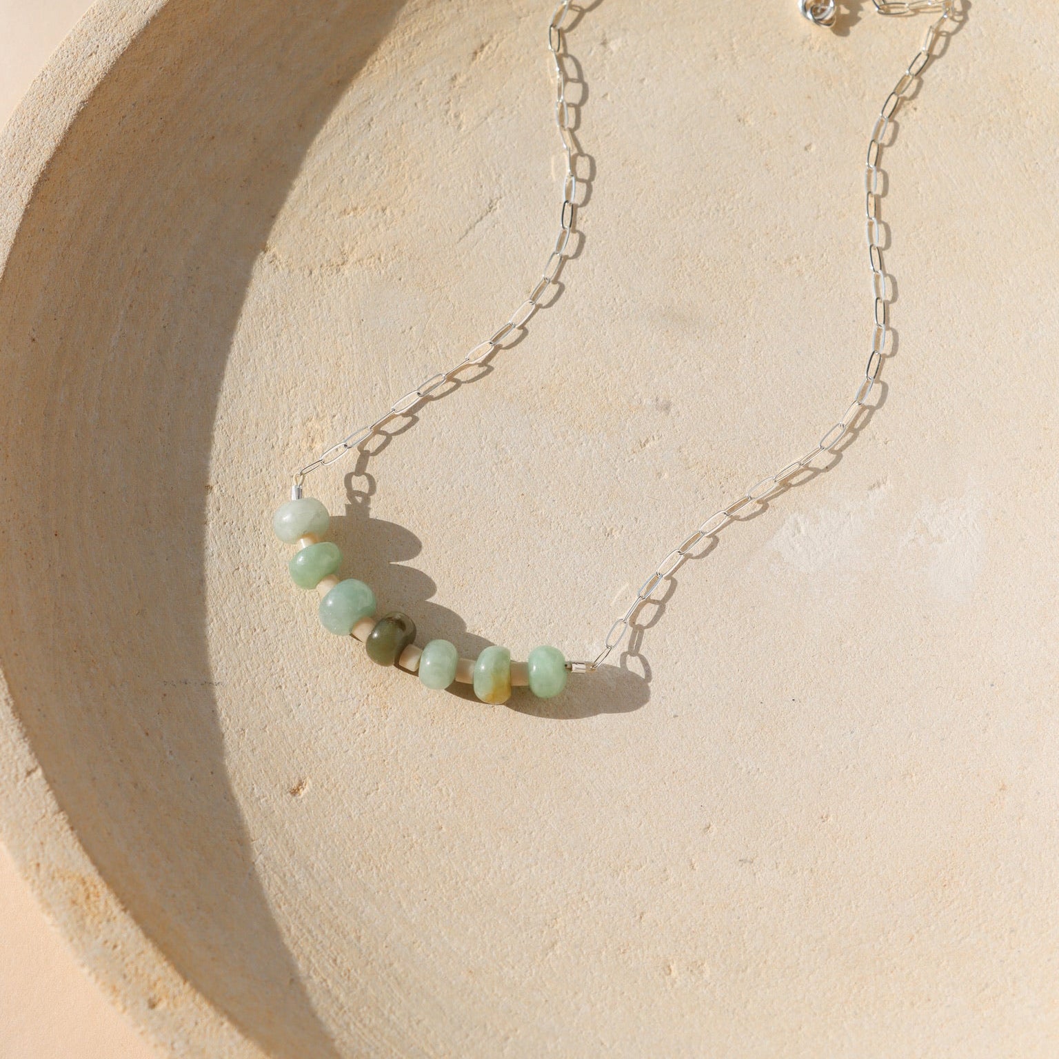 sterling silver paperclip chain necklace with jade beads on a light dish