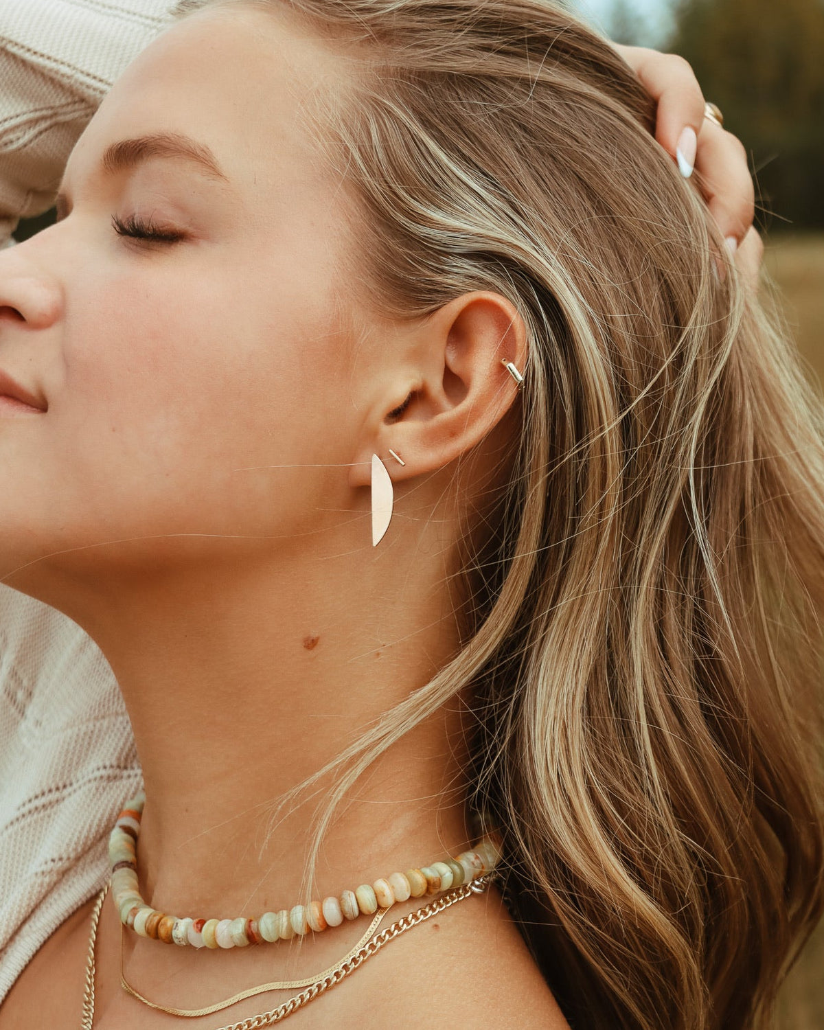 Woman wearing layered gold necklaces with a beaded gemstone necklace and gold earrings outdoors.