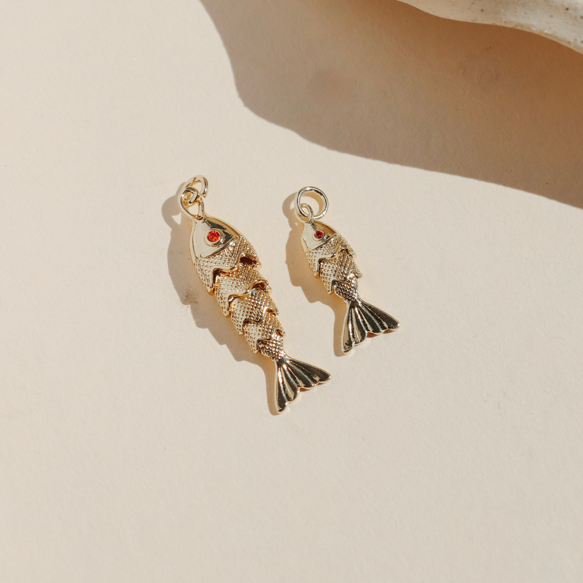 Large and small gold koi fish charms with red crystal eyes displayed on a neutral surface in warm natural light