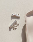 A silver necklace layering clasp with three necklace attachment points laid on a cream backdrop. 