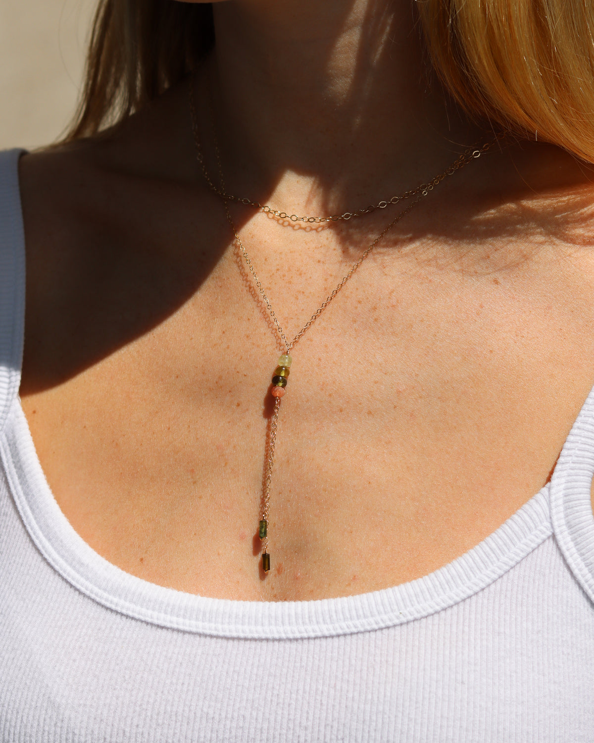 Layered necklace featuring multicolored green and coral gemstone beads with delicate chain tassels.