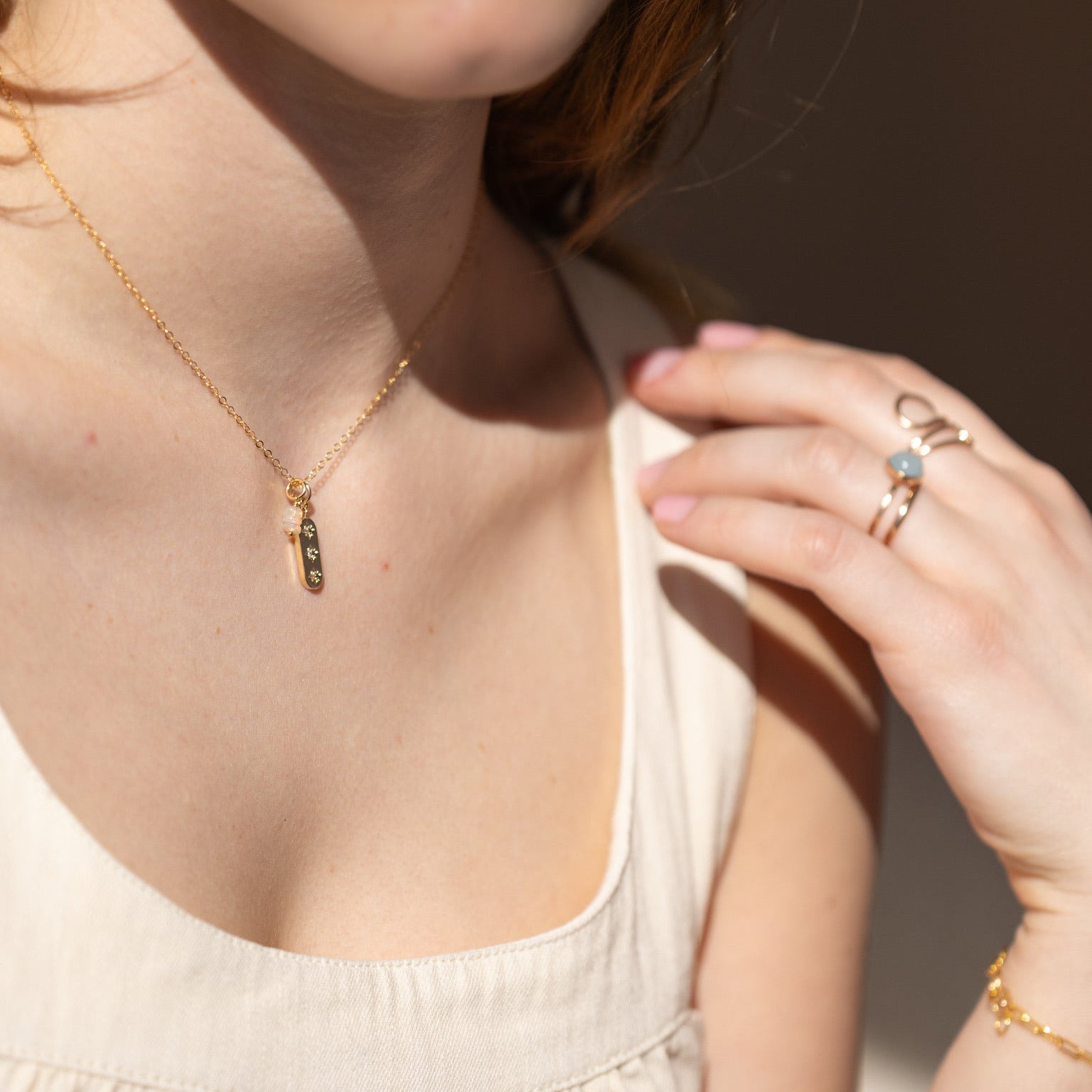 Close-up of model wearing three opals in a minimalist gold bar necklace with stacked opal bead detail