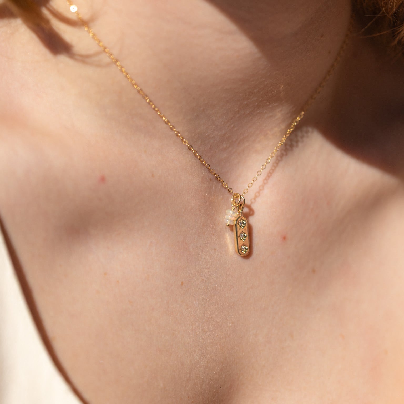 Close-up of model wearing three opals in a minimalist gold bar necklace with stacked opal bead detail