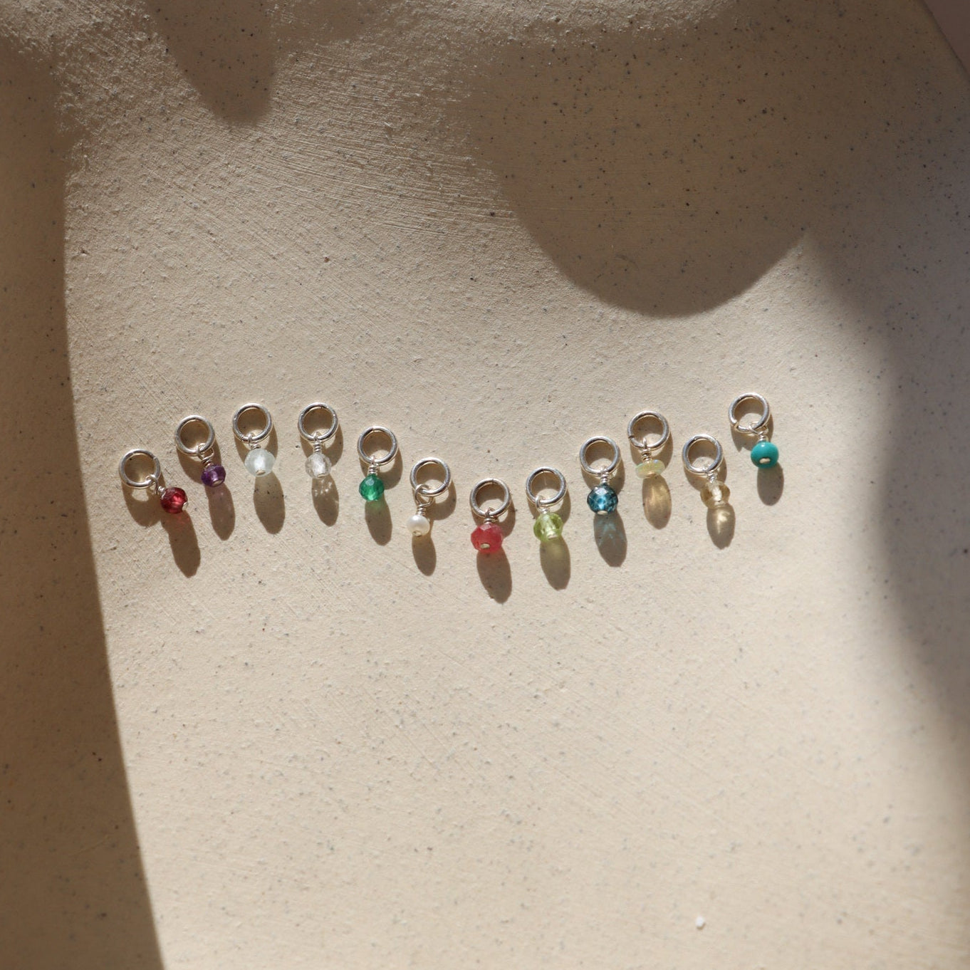 group of tiny birthstones on jump rings in the sun on a light dish